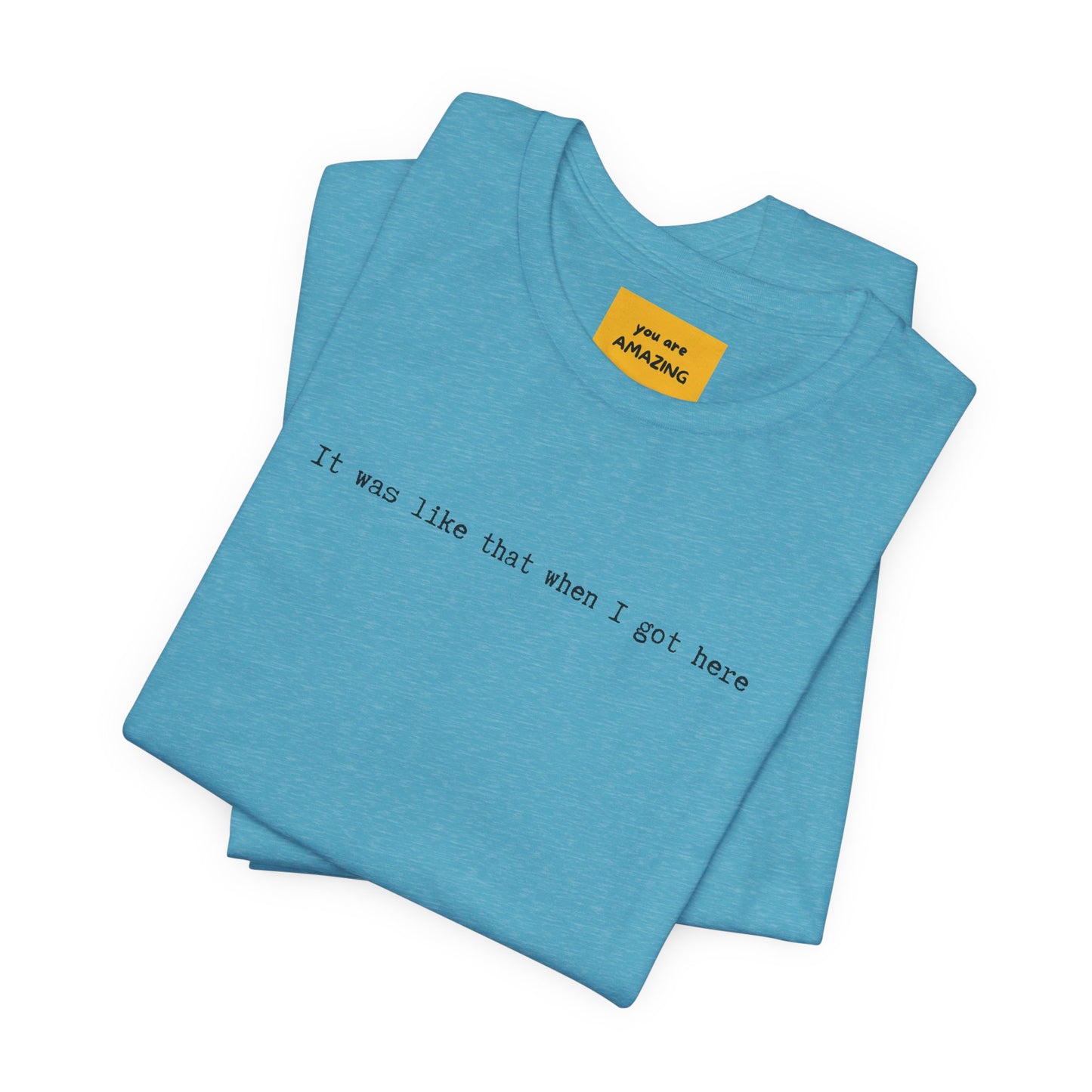 folded blue unisex t-shirt with IT WAS LIKE THAT WHEN I GOT HERE text - funny sarcastic tee and yellow neck label text YOU ARE AMAZING