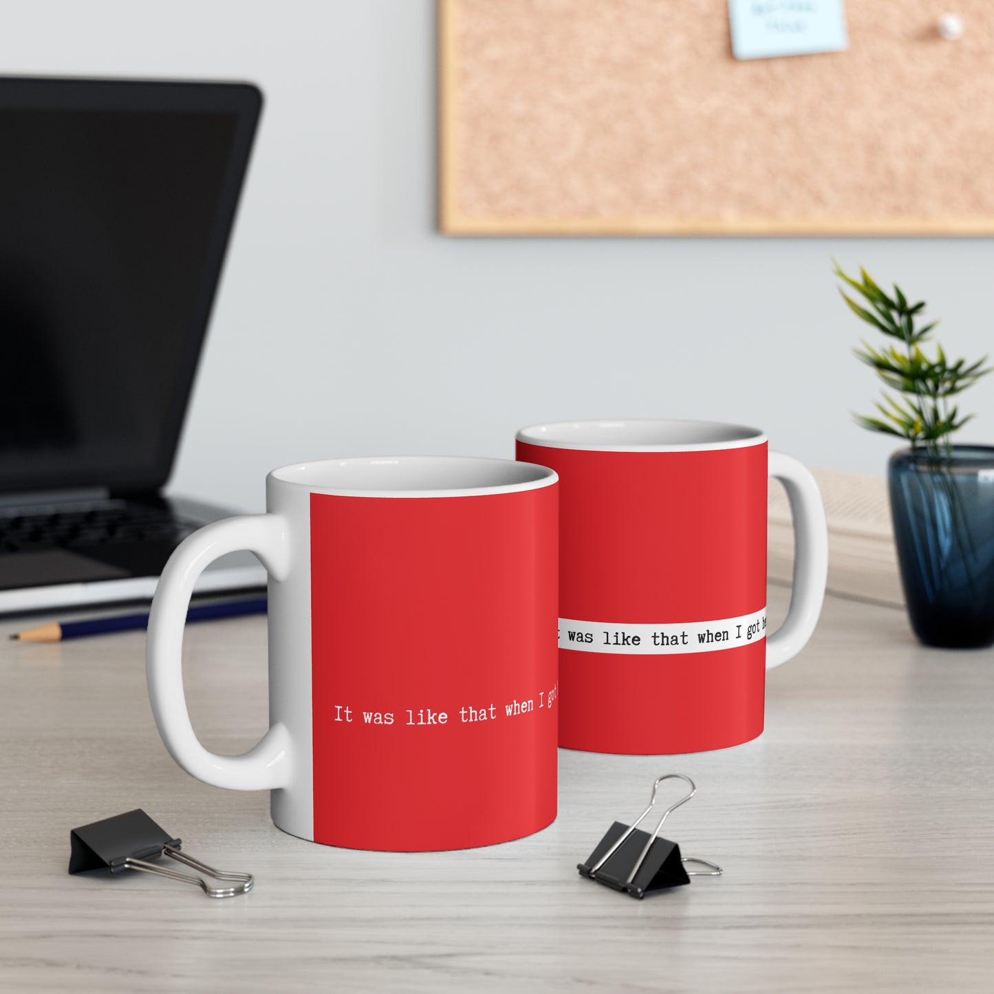 Two red and white mugs with text on a desk with office items.