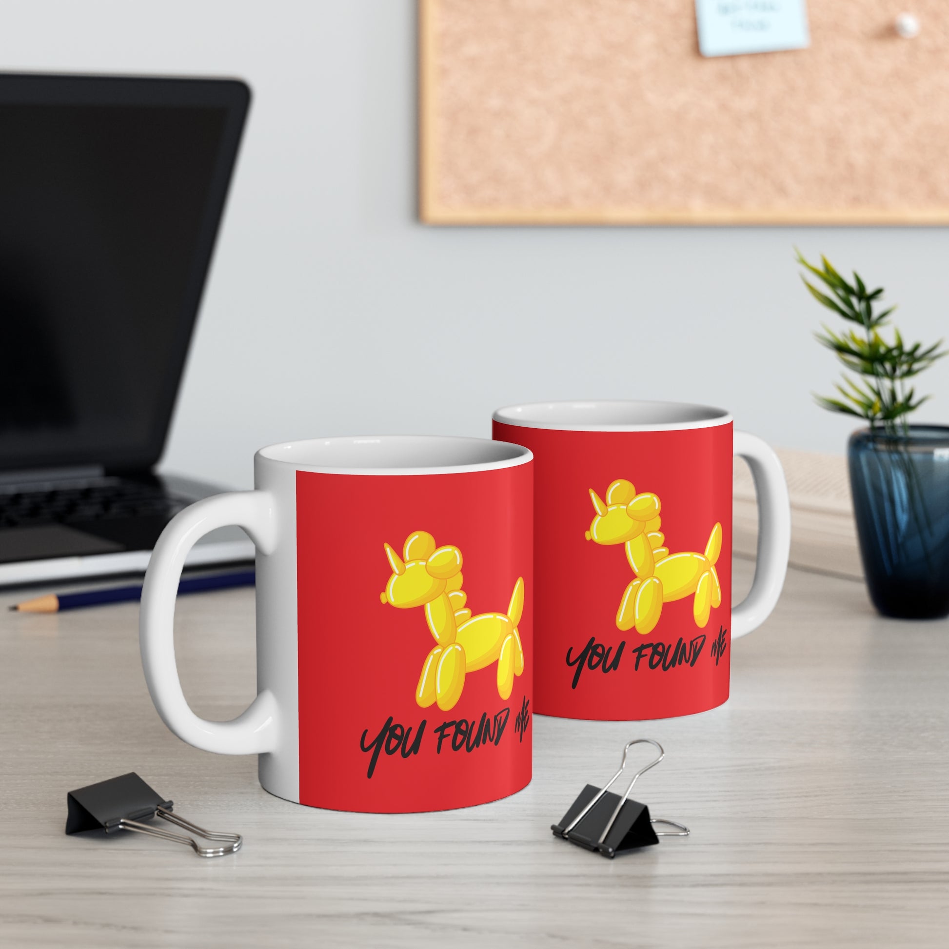 Two red mugs with yellow unicorn ballon animals illustrations on a desk.