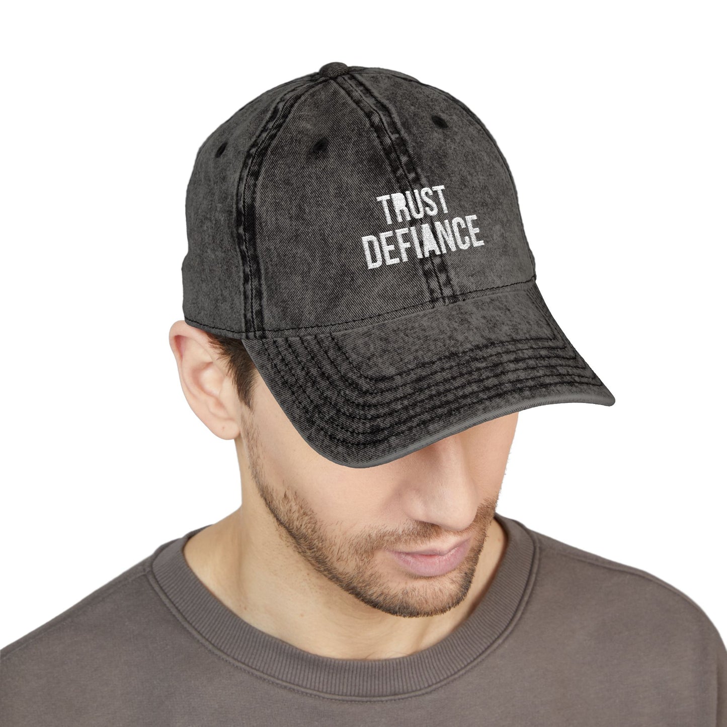 Man wearing a black denim cap with 'TRUST DEFIANCE' text on a white background