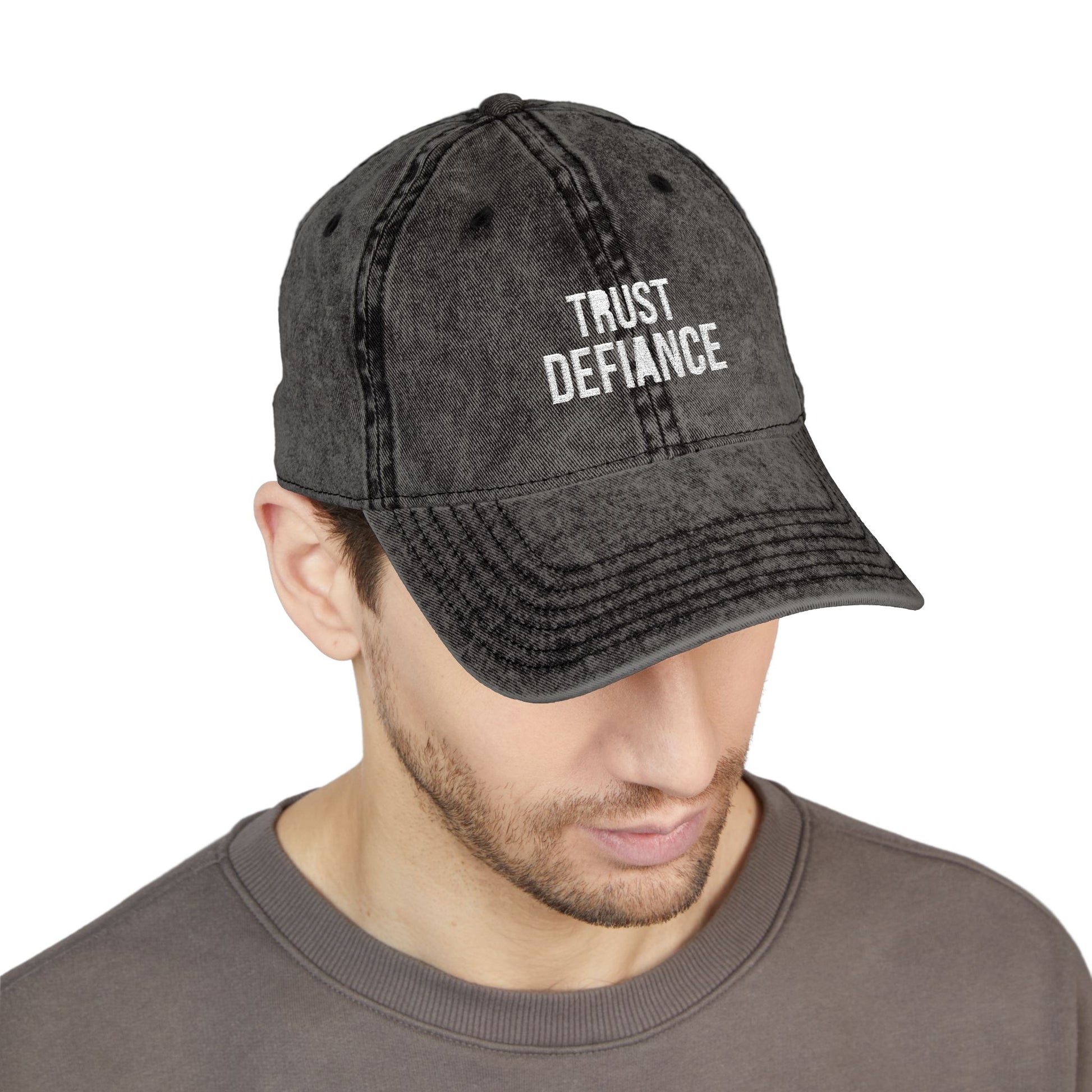 Man wearing a black denim cap with 'TRUST DEFIANCE' text on a white background