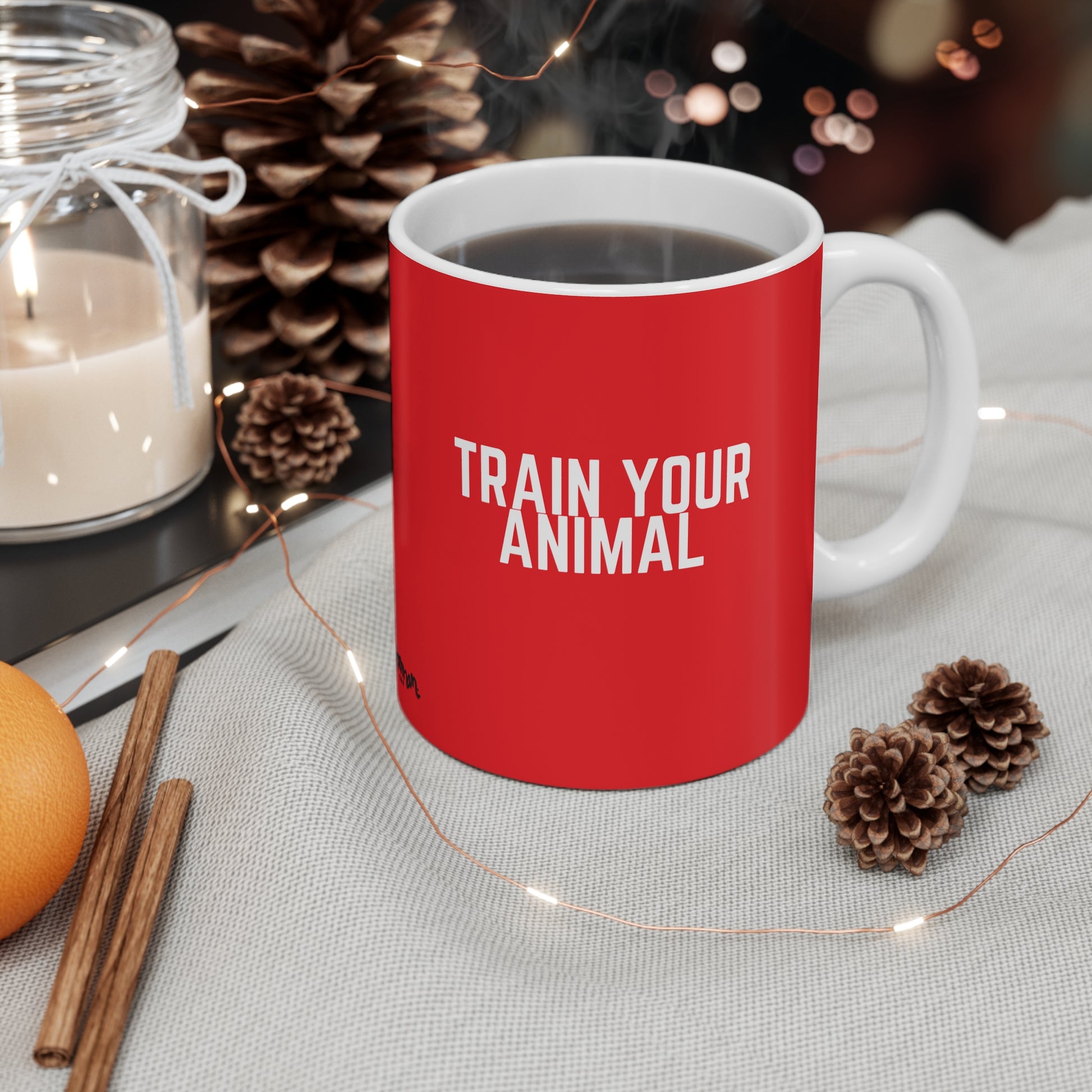 Red mug with 'TRAIN YOUR ANIMAL' text on a table with decorative items