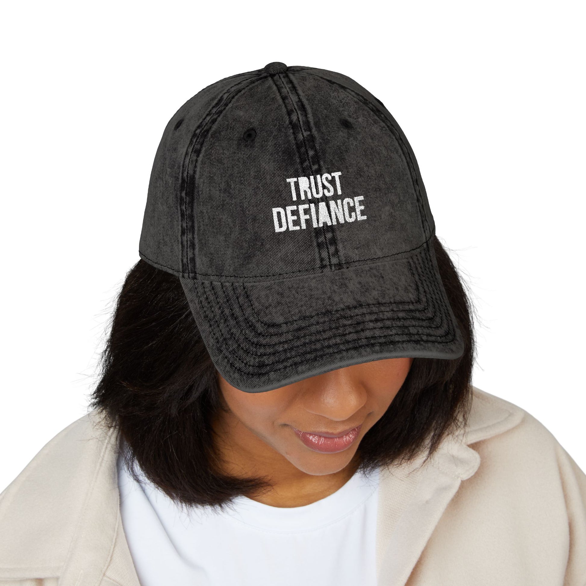 Person wearing a black cap with 'TRUST DEFIANCE' text on a white background